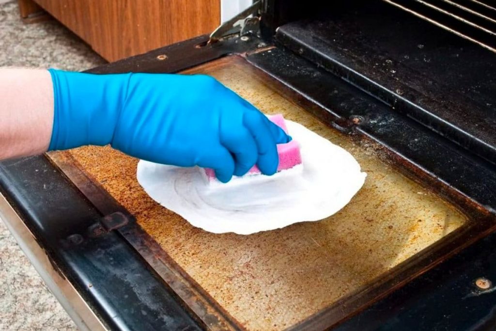 A professional house cleaner scrubbing the inside of a dirty oven.